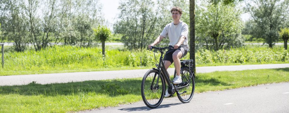 Man op Batavus e-bike op een fietspad met veel groene bomen en planten op de achtergrond