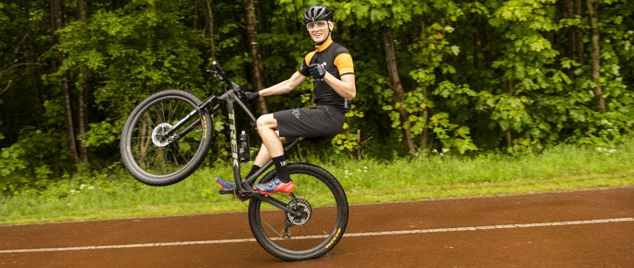 Mountainbiker met 12GO Biking fietsshirt maakt wheelie op zwarte Trek mountainbike en steekt zijn duim op naar de camera