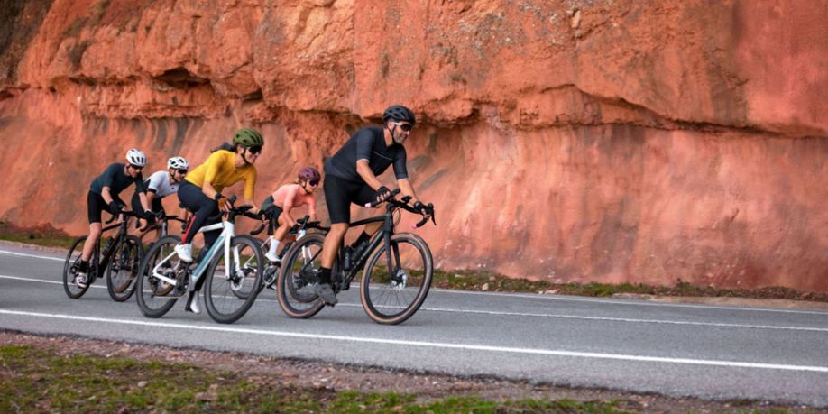 Sfeerbeeld van 5 fietsers met fietscomputers die aan het afdalen zijn op een asfaltweg langs rode rotsen