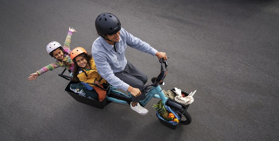Bovenaf shot van man met blauw Trek Fetch longtail op asfalt en twee kinderen achterop waarbij er eentje haar armen uitsteekt