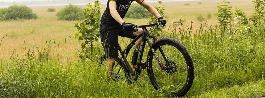Mountainbiker met 12GO Biking fietsshirt op Trek mountainbike door het hoge gras