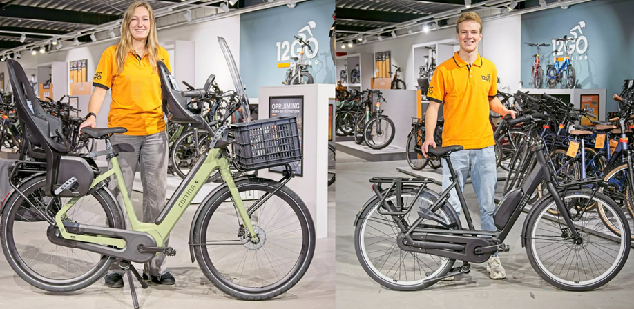 Links een vrouw met 12GO Biking shirt en groene Cortina moederfiets, rechts een man met 12GO Biking shirt zwarte Gazelle moederfiets in de winkel