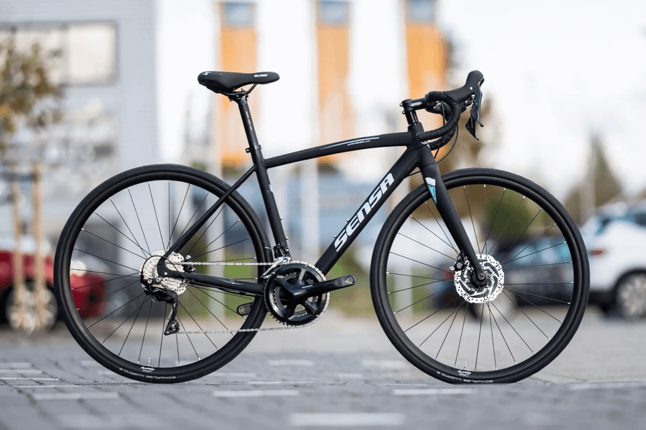 Sensa Latina LTD op het parkeerterrein van 12GO Biking met de oranje 12GO Biking vlaggen op de achtergrond