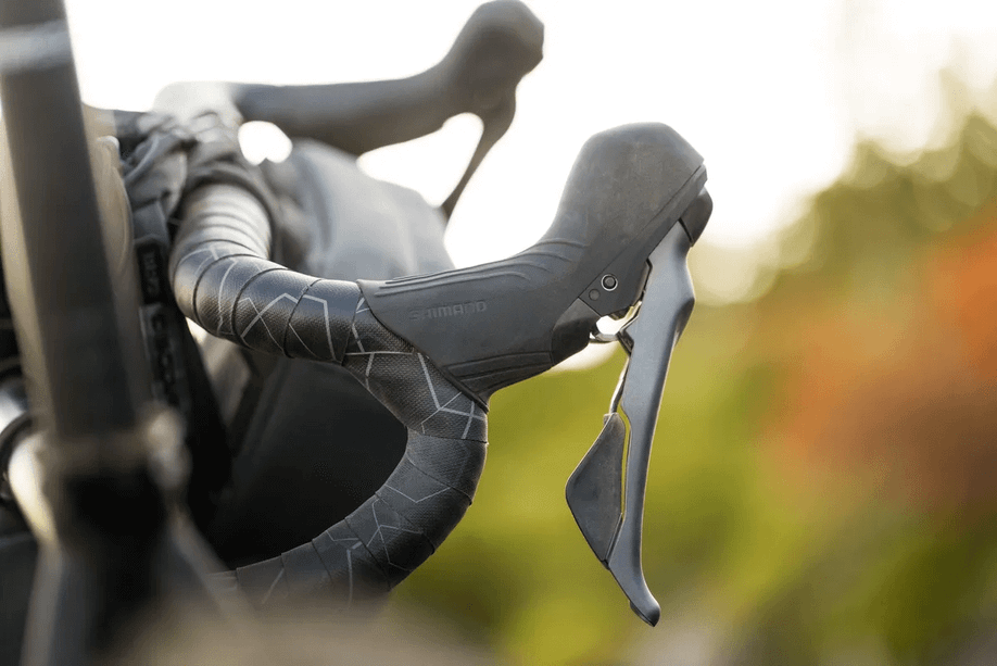 Close-up van Shimano GRX820 shifters op een gravelbike met zwarte stuurlint en een zwarte stuurtas voorop