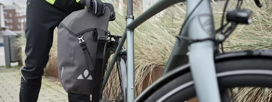 Enkele Vaude fietstas op een grijze fiets in de wintermaanden waarbij een persoon met handschoenen de bovenkant open maakt