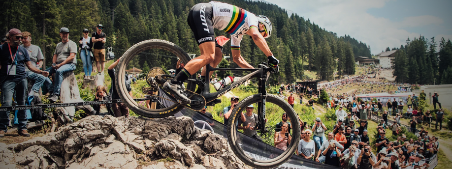 Mountainbiker met WK trui die over rotsen heen gaat voor veel publiek
