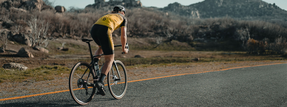 Racefietsers met geel scott fietsshirt op geasfalteerde weg met gele lijn in droog klimaat