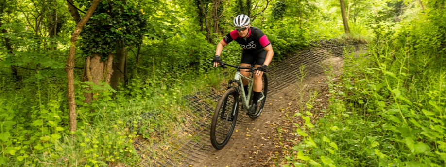 Vrouw met roze 12GO Biking fietsshirt daalt met lichtgroene mountainbike af van aangelegd mountainbikepad in het bos