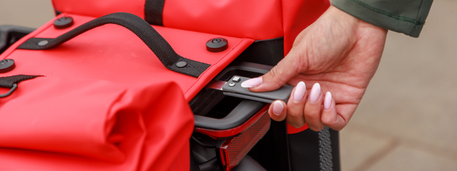 Vrouw houdt hendel van rode dubbele fietstas vast die achterop een bagagedrager gemonteerd zit