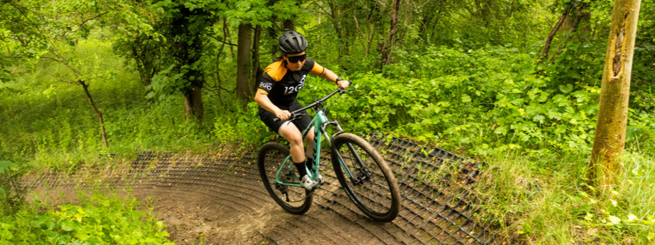 Vrouwelijke fietser met groene Trek mountainbike die een aangelegd mountainbikepad in het bos omhoog fietst tussen al het groen