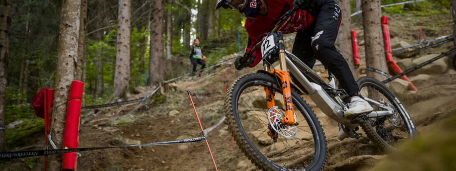 Mannelijke mountainbiker daalt technisch wedstrijd parcours door het bos af met full suspension MTB en oranje Fox voorvork