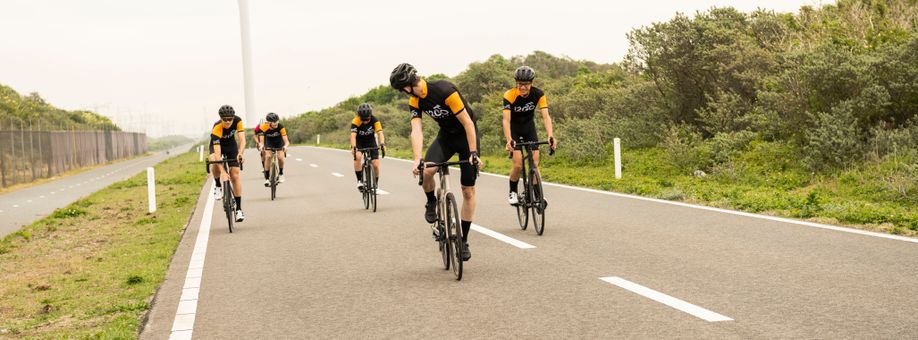 5 fietsers met 12GO Biking fietskleding op een autoweg waarbij ze allemaal wat uit elkaar rijden richting de camera