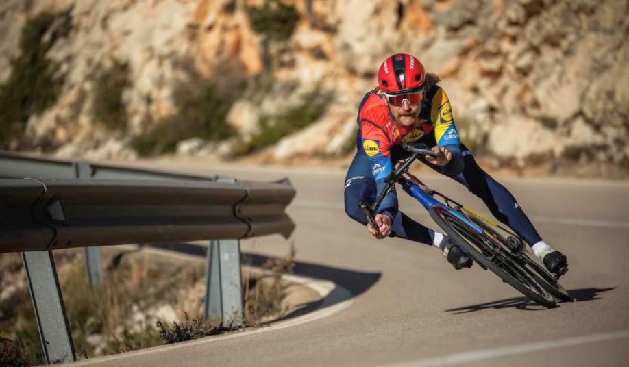 Quinn Simons met zijn professionele Lidl-Trek fietskleding die enorm schuin in de bocht hangt met zijn racefiets tijdens een afdaling