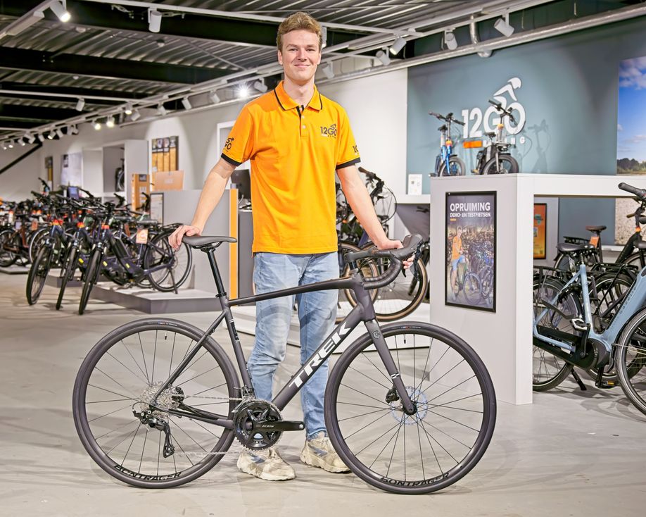 Medewerker met 12GO Biking shirt met de Trek Domane AL 5 Gen 4 in zijn handen in de showroom van 12GO Biking