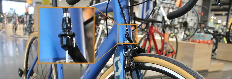 Blauwe Scott racefiets met ingezoomd beeld op de aansluiting van de velgremmen in de showroom van 12GO Biking