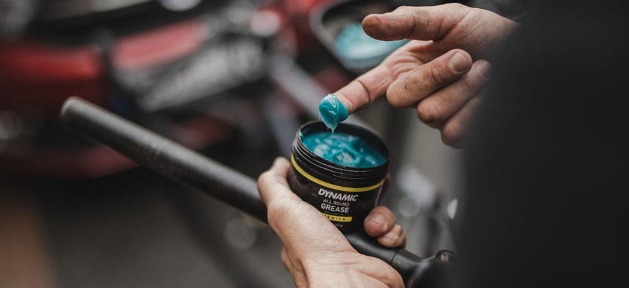 Persoon met een blauwe vingertop met montagepasta van Dynamic All Round Grease potje in zijn andere hand