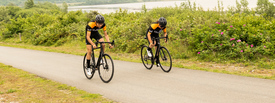 Mannelijke en vrouwelijke racefietsers op endurance racefietsen die sprinten over een fietspad lang struiken en een meer op de achtergrond