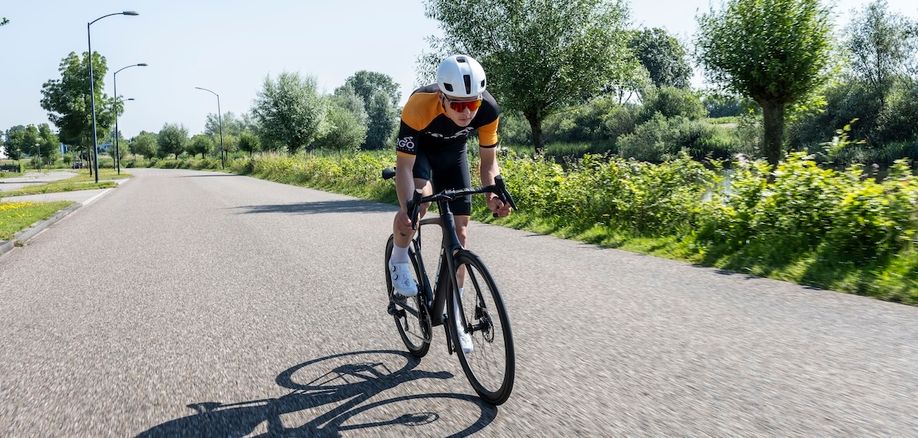Racefietser op een Trek Madone aero racefiets met 12GO Biking fietskleding die over een asfaltweg snelheid maakt door uit het zadel te komen