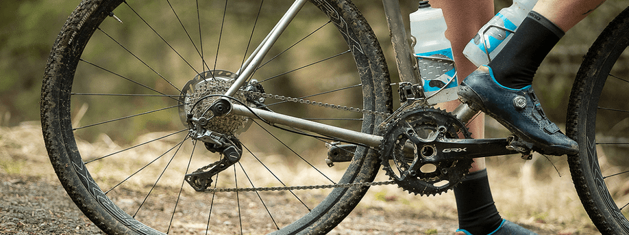 Shimano GRX groepset op een grijze gravelbike met vieze banden en twee witte bidons met water