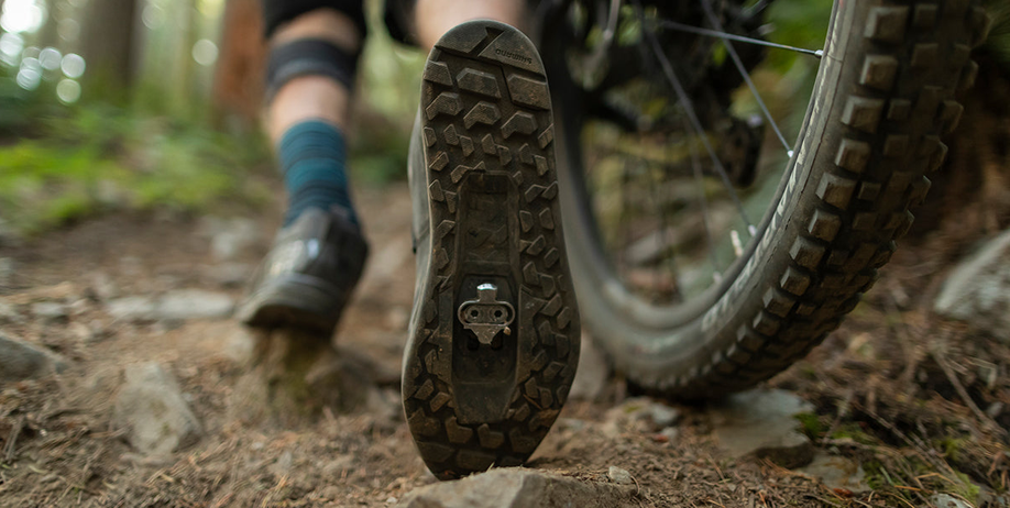 Onderkant van een schoen met MTB-schoenplaatjes in de inkeping op een bospad met de mountainbike