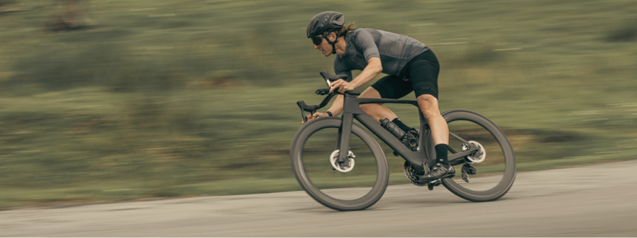 Fietser met volledig zwarte aero racefiets en zwarte kleding die op snelheid door de bocht gaat en leunt