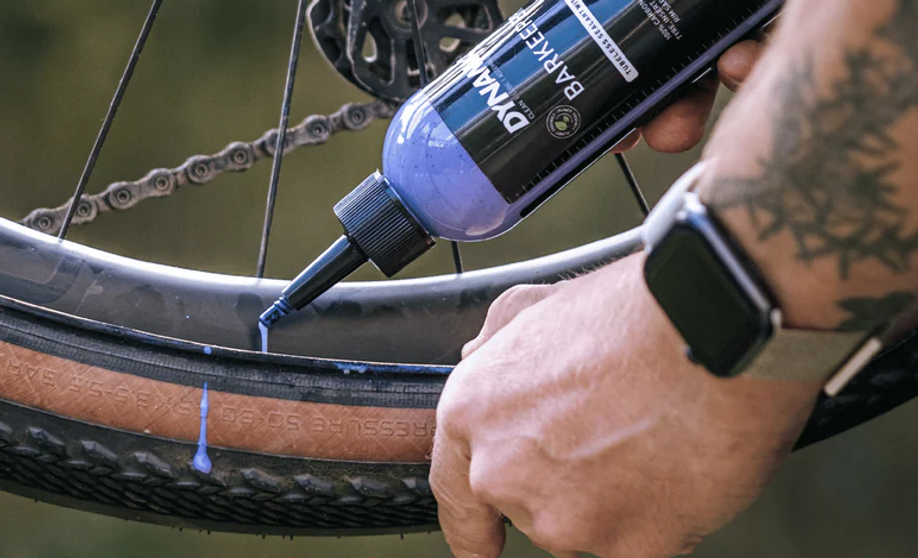 Persoon met Apple Watch voegt Dynamic Barkeeper Tubeless Sealant toe aan een gravelbuitenband en morst een beetje op het band