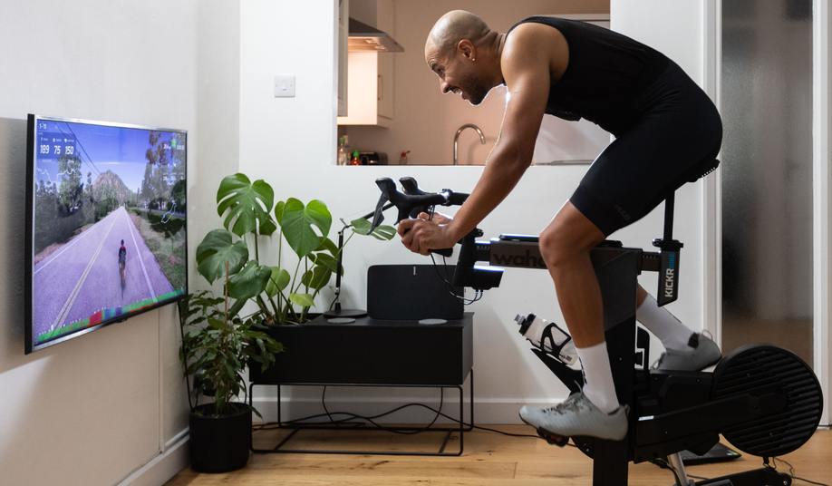 Fietser op Wahoo Kickr fietstrainer in woonkamer met tv-scherm voor zich waarop hij een training uitvoert