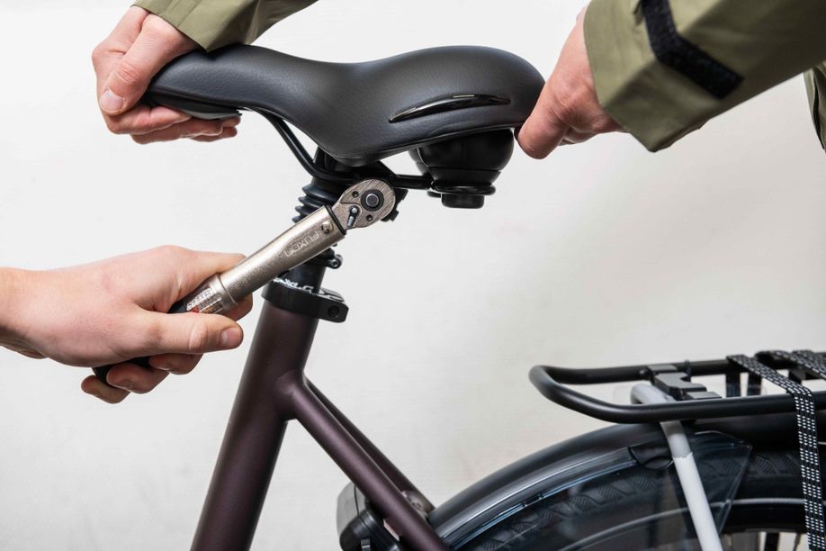 1 persoon houdt zadel vast om de juiste zadelhoek te bepalen terwijl ander persoon het zadel los- of vastdraait met gereedschap