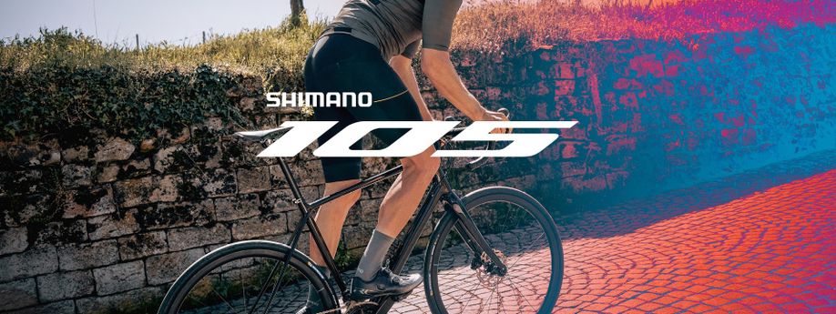 Fietser stat op pedalen en klimt een kasseienstraat op met racefiets met het Shimano 105 logo in het midden bovenop geplaatst