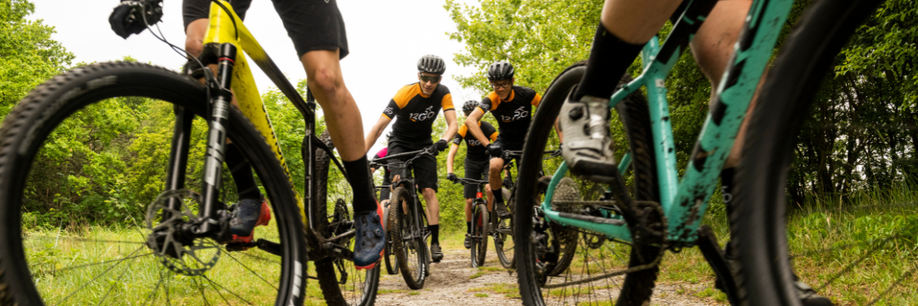 Groep mountainbikers rijden 2 aan 2 richting de camera om aan beide kanten te passeren terwijl ze op een zandpad fietsen