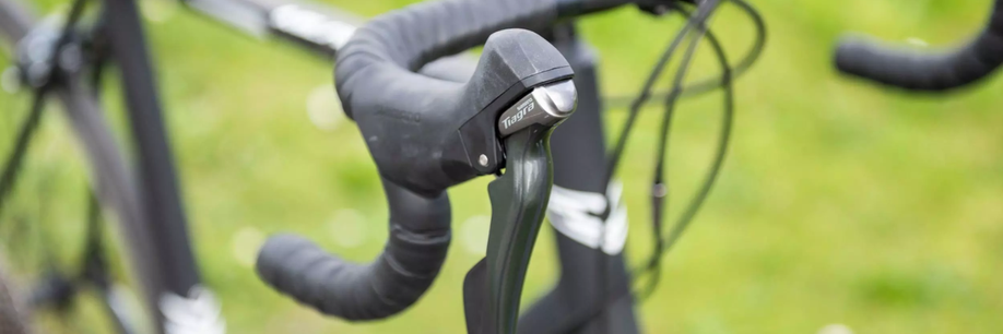 Mechanische shifter op een zwarte racefiets met veel kabels in het zicht voor groen gras