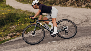 Vrouw met donkergroene Liv racefiets die scherp een bocht in hangt tijdens het afdalen over het asfalt