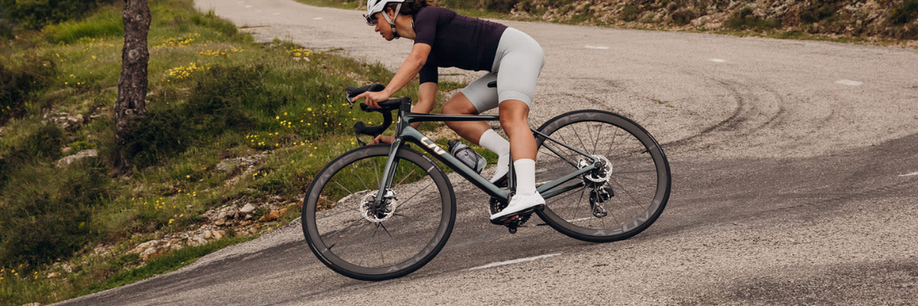 Vrouw met donkergroene Liv racefiets die scherp een bocht in hangt tijdens het afdalen over het asfalt