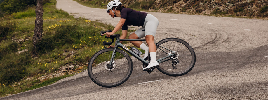 Vrouw met donkergroene Liv racefiets die scherp een bocht in hangt tijdens het afdalen over het asfalt