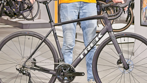 Persoon met blauwe spijkerbroek houdt de Trek Domane AL 5 Gen 4 vast in de showroom van 12GO Biking