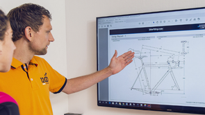 Medewerker van 12GO Biking legt op het scherm aan klant met roze shirt uit hoe de verdelingen van het frame moeten zijn