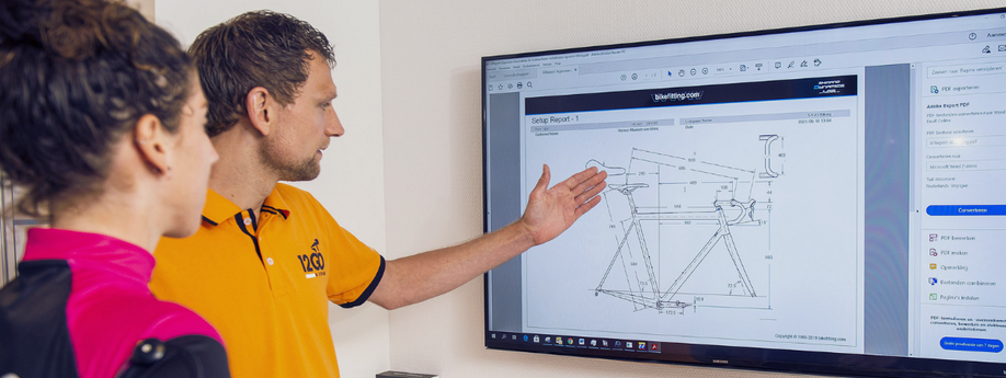 Medewerker van 12GO Biking legt op het scherm aan klant met roze shirt uit hoe de verdelingen van het frame moeten zijn