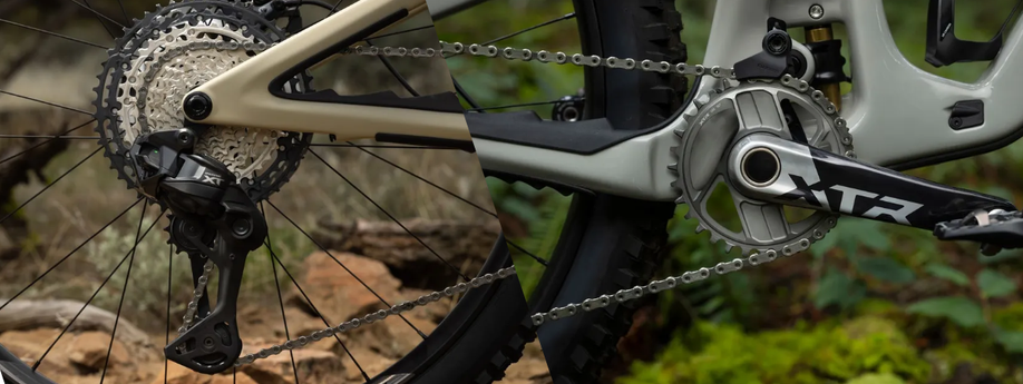 Links een Shimano Deore XT cassette en achterderailleur op een gouden mountainbike, rechts een Shimano XTR crankstel op een grijze mountainbike