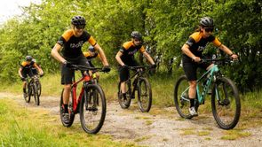 Groep 12GO Biking mountainbikers met 12GO fietskleding die met hun mountainbikers een heuvel lang de bomen omhoog rijden