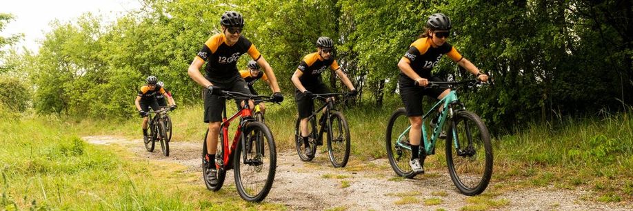 Groep 12GO Biking mountainbikers met 12GO fietskleding die met hun mountainbikers een heuvel lang de bomen omhoog rijden