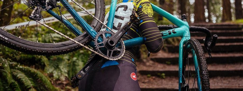 Man loopt met blauwgroene Trek cyclocrosser de trappen van een bos omhoog met aan de zijkant een wit lint met Trek logo's