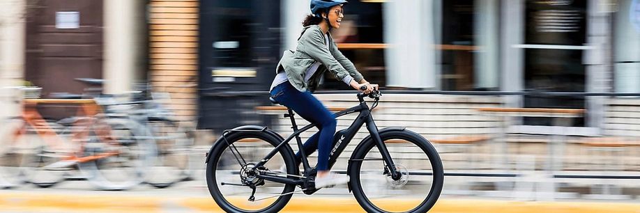 Vrouwelijke fietser met helm op e-bike rijdt snel voorbij huizen met fietsen, bankjes en een hek op de stoep met gele rand