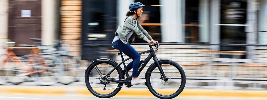 Vrouwelijke fietser met helm op e-bike rijdt snel voorbij huizen met fietsen, bankjes en een hek op de stoep met gele rand