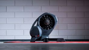 Elite Direto XR-T fietstrainer op een rode Elite trainermat met een betonblokken muur op de achtergrond