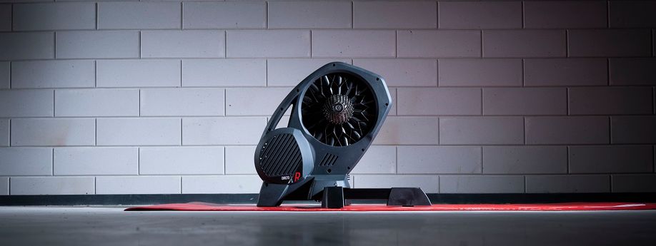 Elite Direto XR-T fietstrainer op een rode Elite trainermat met een betonblokken muur op de achtergrond