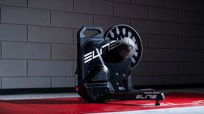 Elite Suito-T fietstrainer op een rode Elite trainermat voor een betonnen getegelde muur