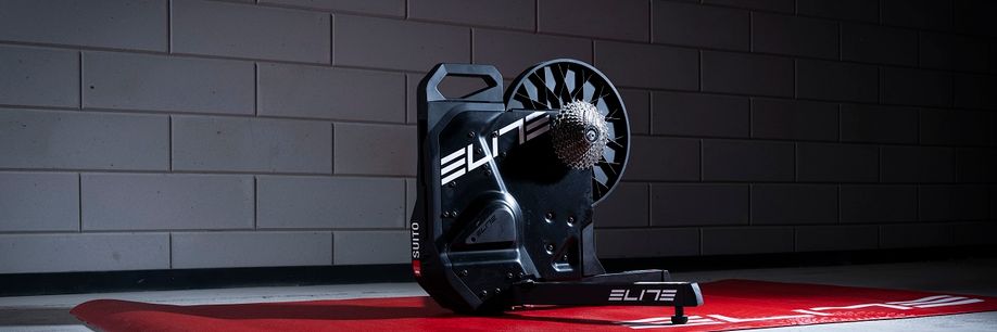 Elite Suito-T fietstrainer op een rode Elite trainermat voor een betonnen getegelde muur