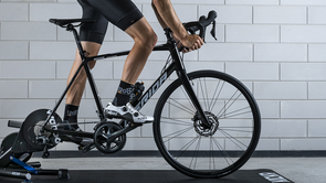 Fietser met 12GO Biking sokken rijdt op de Wahoo Kickr V6 met Merida racefiets voor betonnen muur