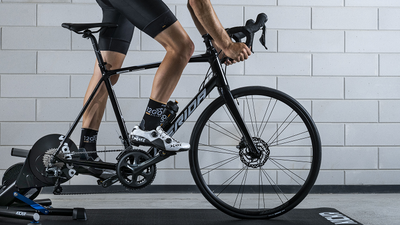 Fietser met 12GO Biking sokken rijdt op de Wahoo Kickr V6 met Merida racefiets voor betonnen muur