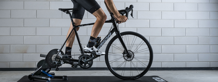 Fietser met 12GO Biking sokken rijdt op de Wahoo Kickr V6 met Merida racefiets voor betonnen muur